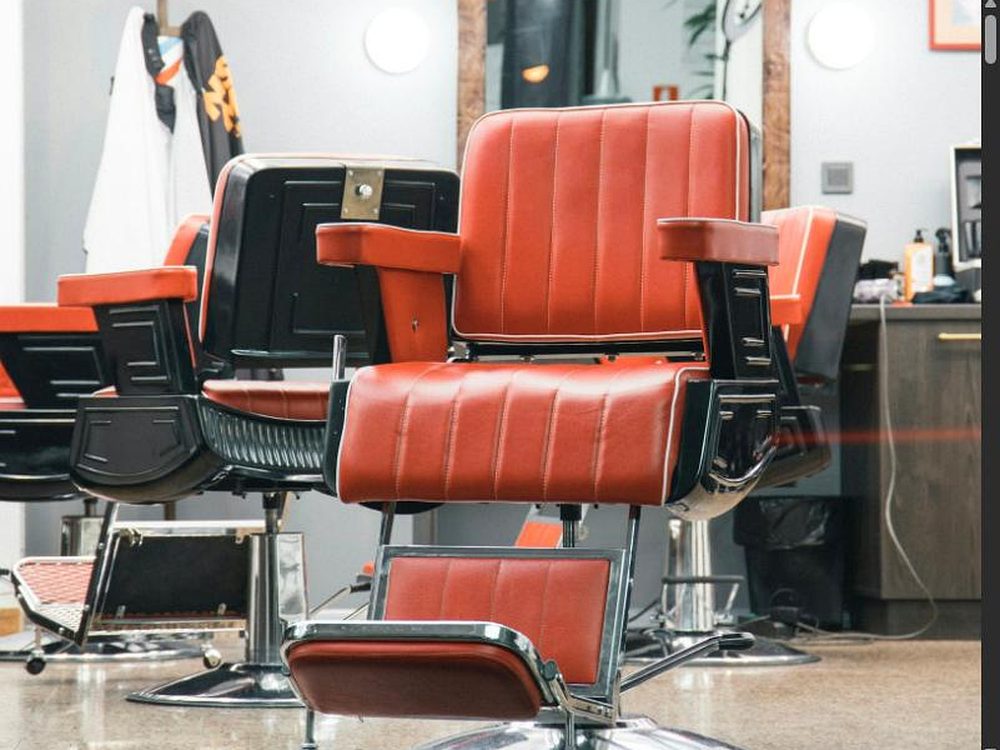 Reihe roter Barber-Ledersessel im Salon vor Spiegeln mit Gl&uuml;hbirnen im Retro-Look