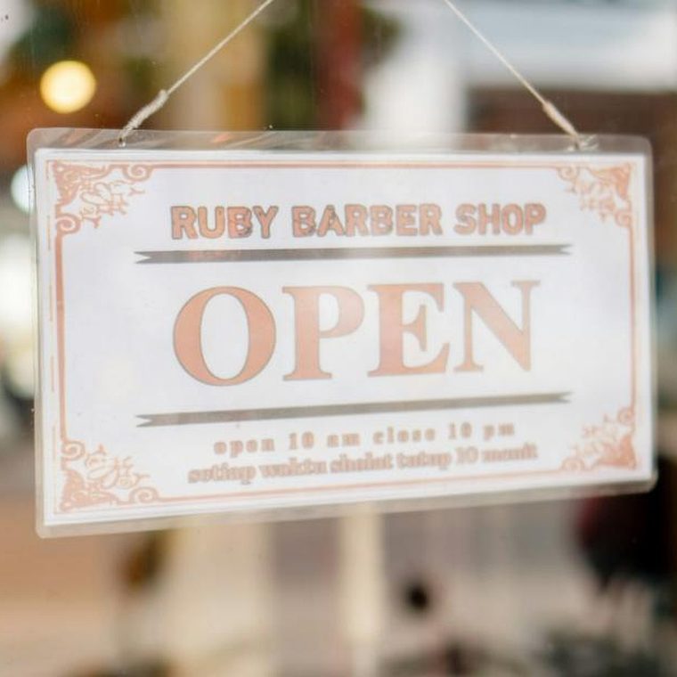 &bdquo;OPEN&ldquo;-Schild im Schaufenster, dahinter unscharf der warm beleuchtete Salon