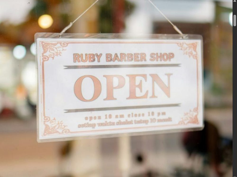 &bdquo;OPEN&ldquo;-Schild im Schaufenster, dahinter unscharf der warm beleuchtete Salon