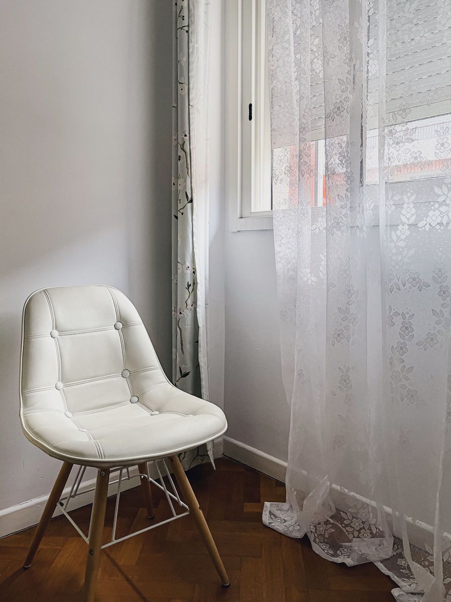 Weißer Sessel am Fenster hinter einem Spitzenvorhang