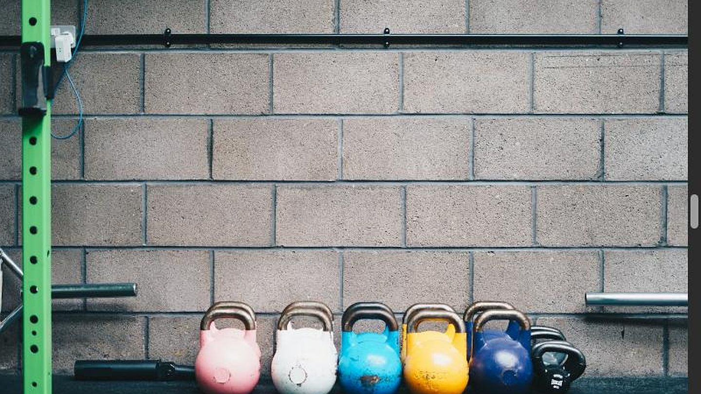 Reihe bunter Kettlebells vor einer Betonwand, daneben ein grüner Rack-Ständer im industriellen Look