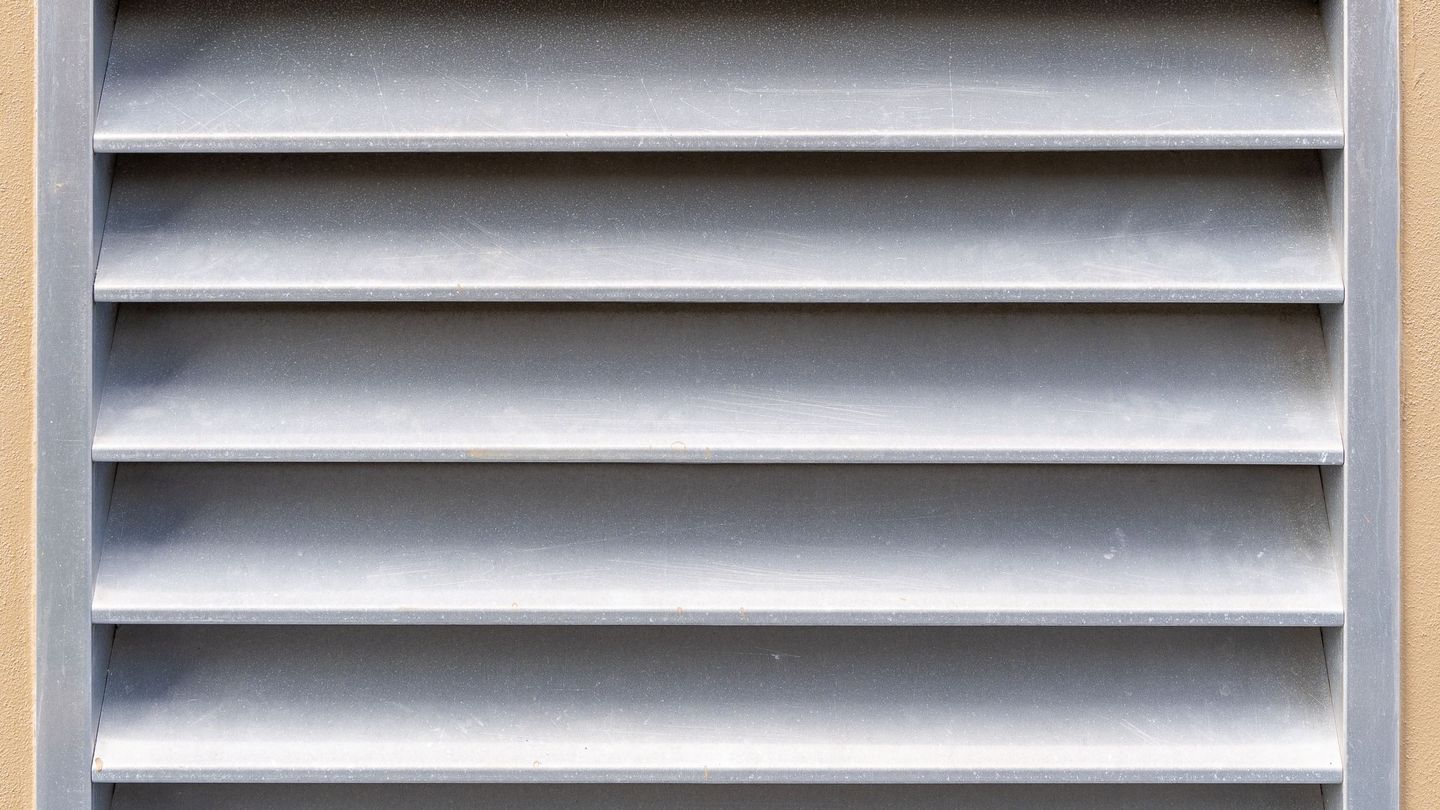 Metal vent grille on a beige stucco wall