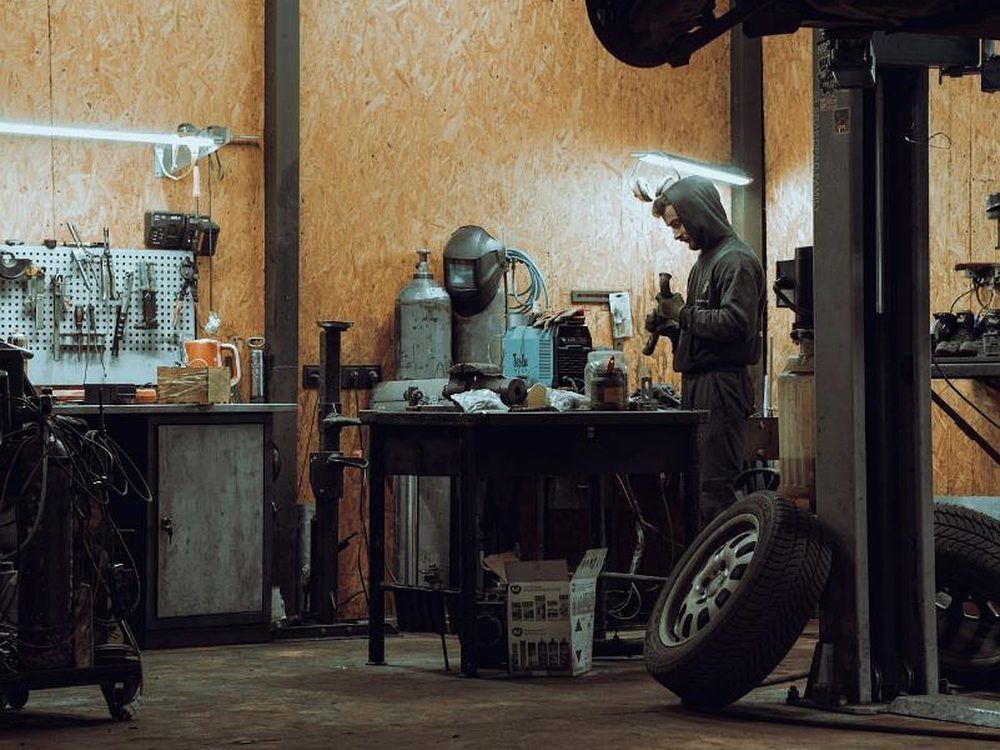Mechaniker an der Werkbank, daneben ein angehobenes Fahrzeug auf der Hebebühne