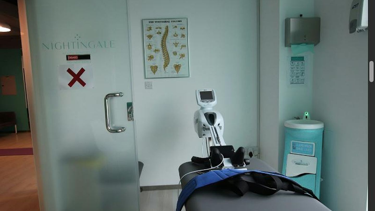 Behandlungskabine mit Therapiegerät und Gurten auf der Liege, Wirbelsäulen-Poster an der Wand und Milchglastür