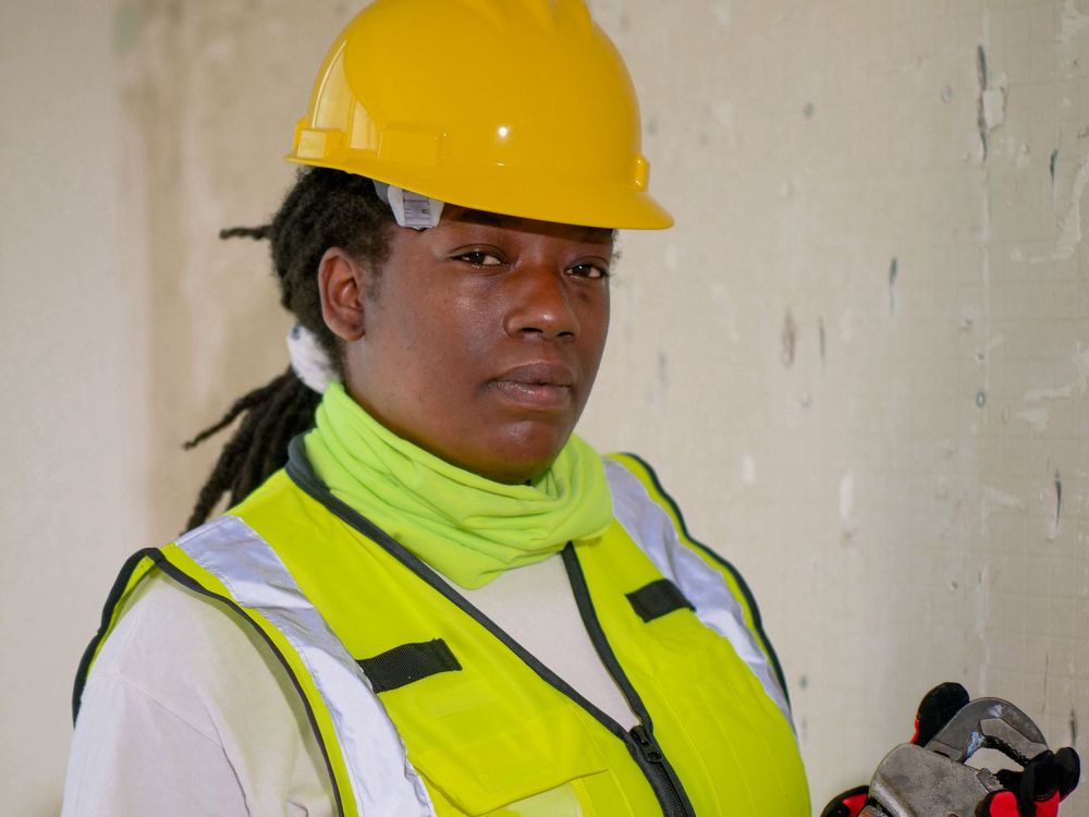 A plumber in safety gear holding a pipe wrench
