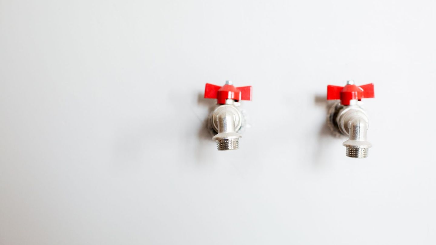 Two shutoff valves with red handles on a white wall