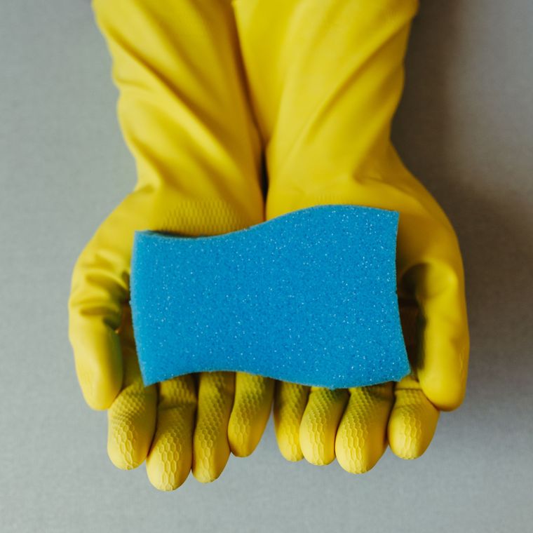 Hände in gelben Handschuhen halten einen blauen Schwamm