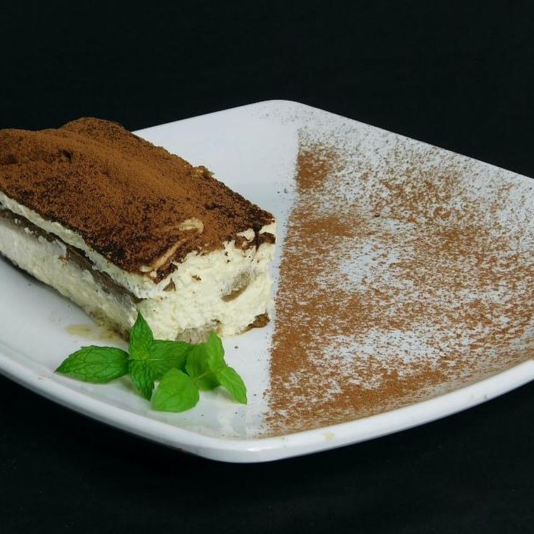 Angerichtetes Stück Tiramisù auf weißem Teller mit Minze und Kakaobestäubung