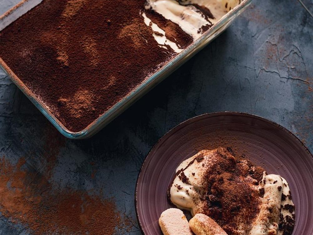 Hausgemachtes Tiramisù in der Auflaufform und in einer Schale auf dunklem Stein