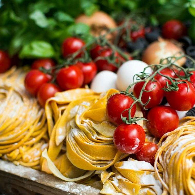 Rohe Tagliatelle-Nester mit Kirschtomaten, Basilikum und Eiern auf einem Holzbrett