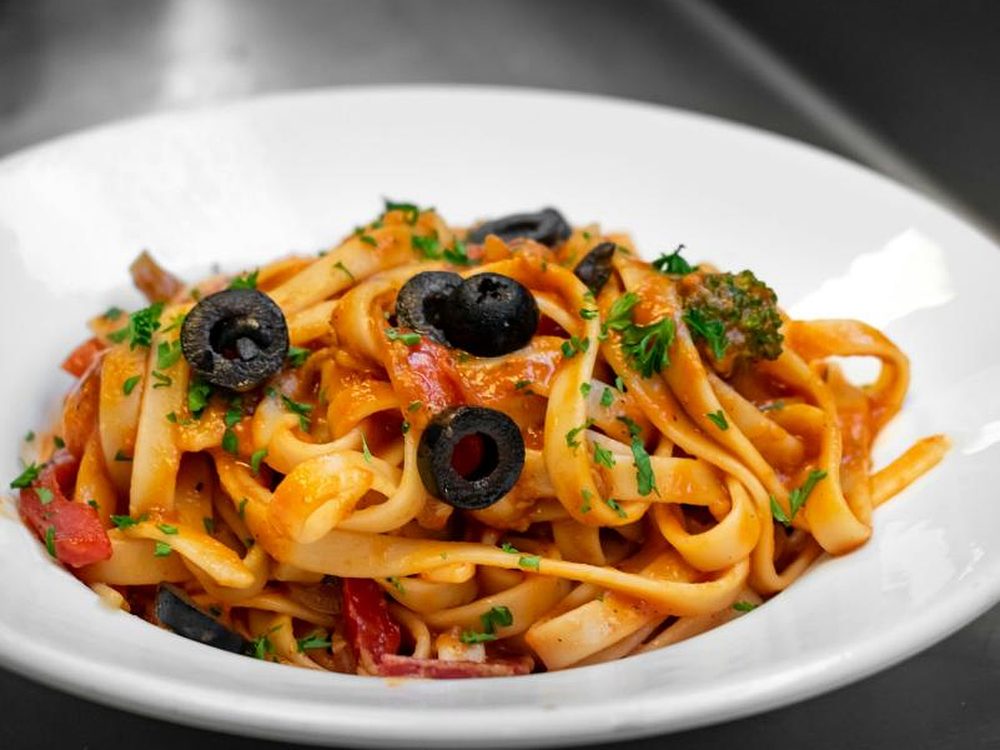 Angerichteter Teller Tagliatelle in Tomatensauce mit schwarzen Oliven und Brokkoli
