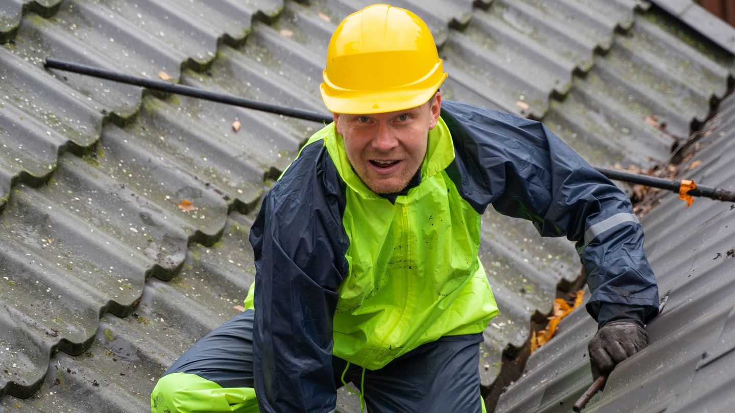 Roofer wearing a hard hat and safety harness on a pitched roof