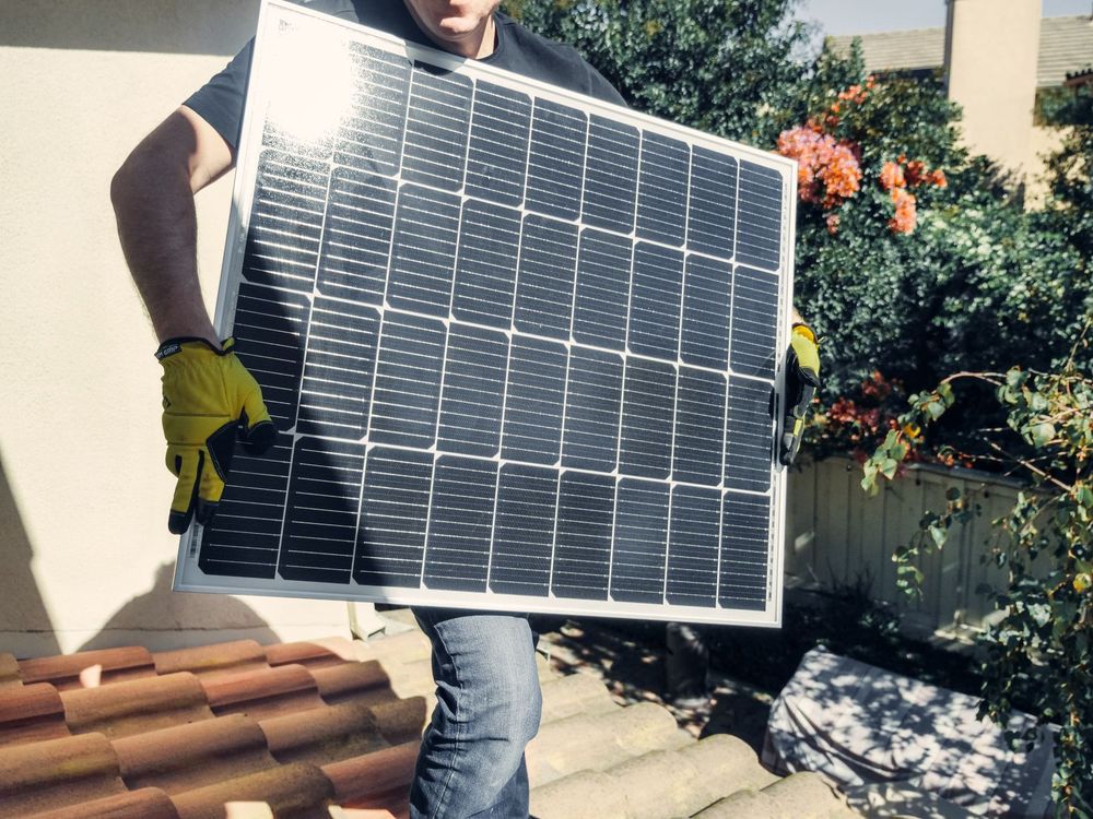 Installer carrying a solar panel across a tile roof
