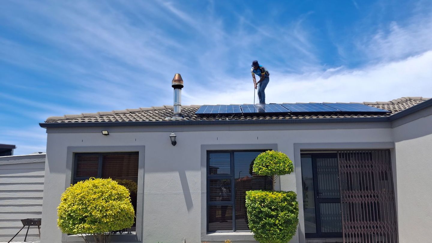 Installer on the roof of a single-story house fitting solar panels under a blue sky