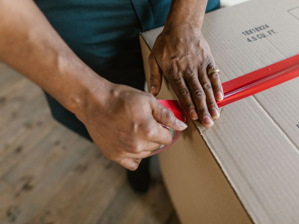 Hände kleben Packband auf einen Karton