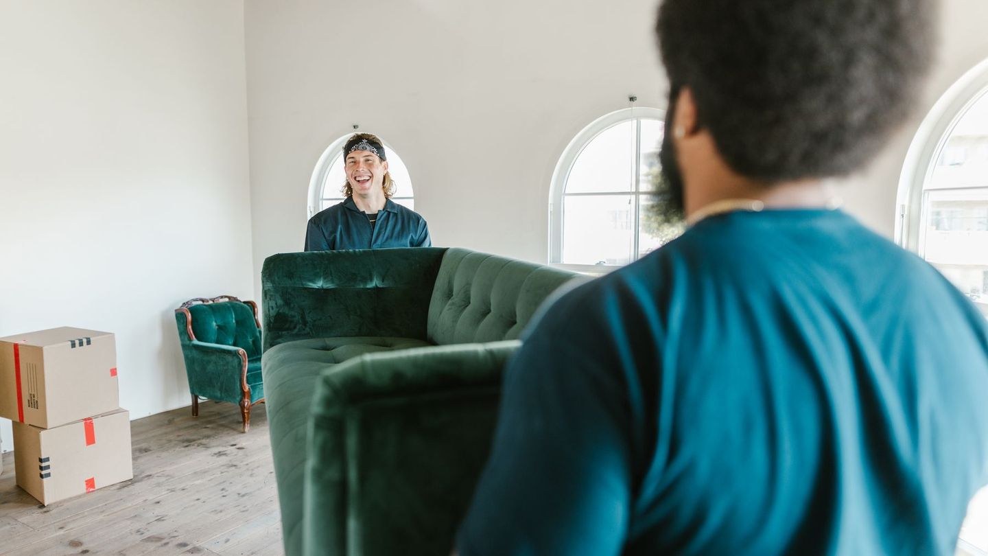 Zwei Möbelpacker tragen ein grünes Sofa durch eine helle Wohnung